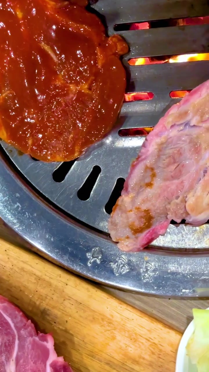 Tampilan dekat daging yang sudah dimarinasi sedang dipanggang di BBQ Korea. Penjepit digunakan untuk membalik daging di atas panggangan panas