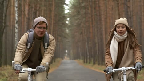 Front-View-Of-A-Couple-Wearing-Winter-Clothes-Riding-Bikes-In-The-Forest-While-Raining