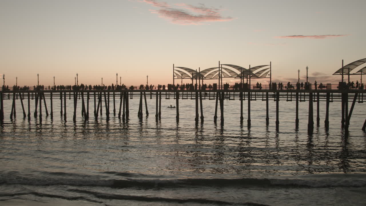 Metraje cinematográfico 4K del muelle de Redondo Beach con un paneo lento de izquierda a derecha, capturando la luz del atardecer sobre el Océano Pacífico, gente pescando y paseando, un cielo vibrante, olas del océano y el pintoresco sur de California.