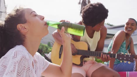 feliz mujer biracial bebiendo cerveza con diversos amigos riendo en la fiesta de la piscina