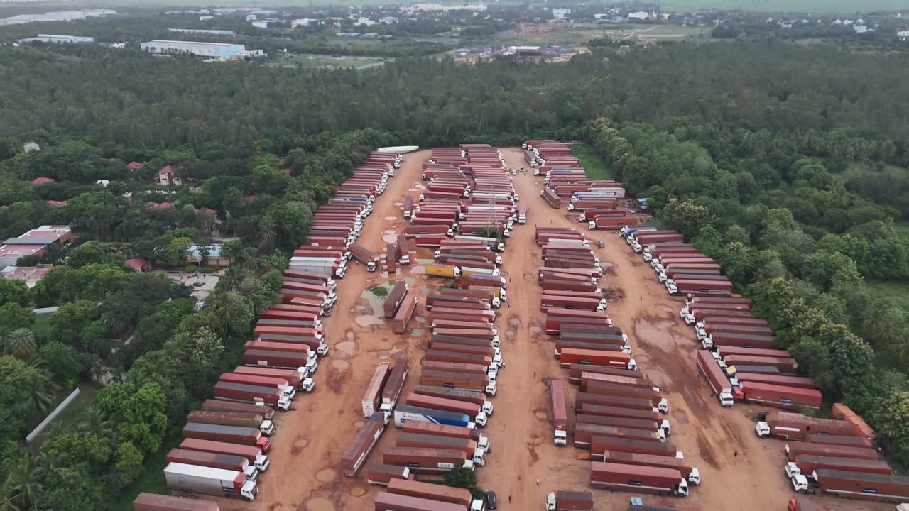 Cinematic drone view of an immense truck staging area with long, neat rows of commercial vehicles parked on dirt. Perfect for freight, transport, and industry