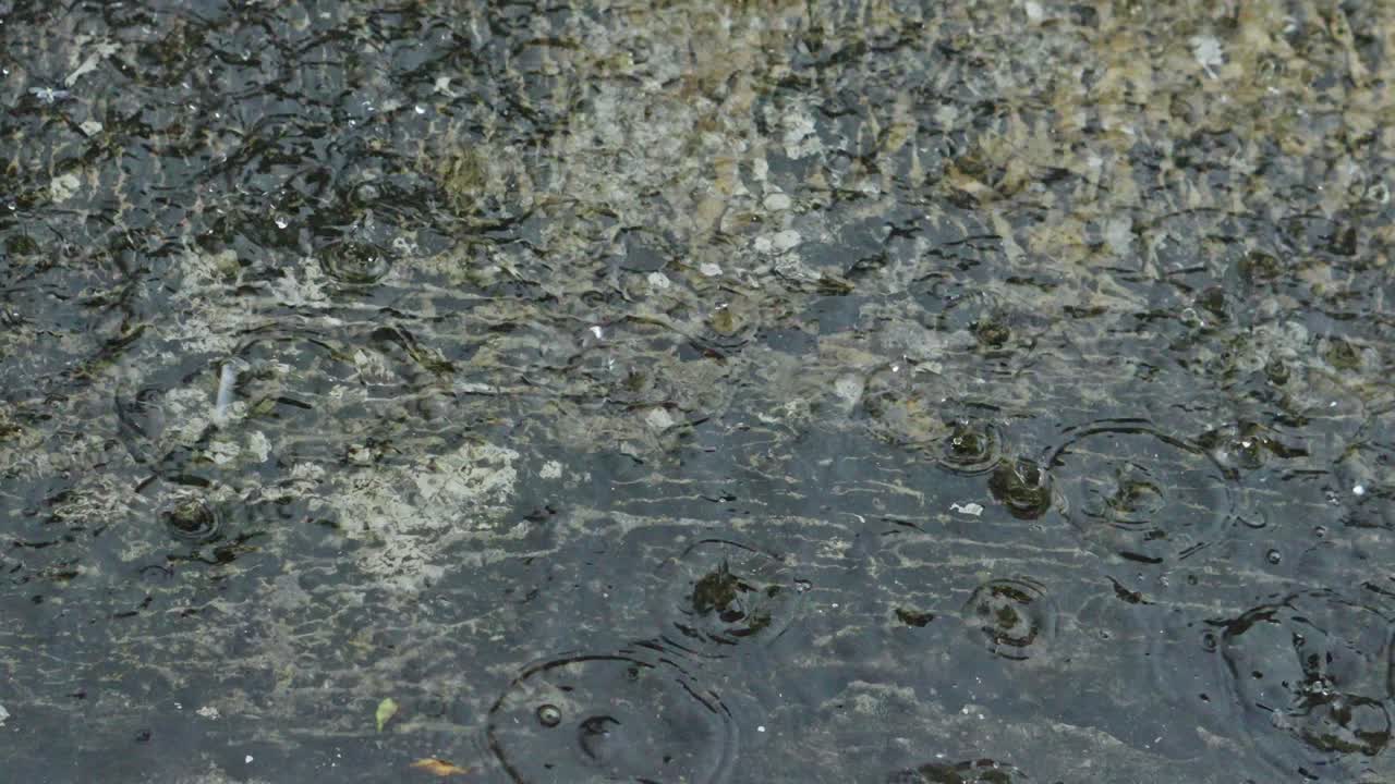 Tetesan hujan menghantam tanah beton yang tergenang saat hujan deras.