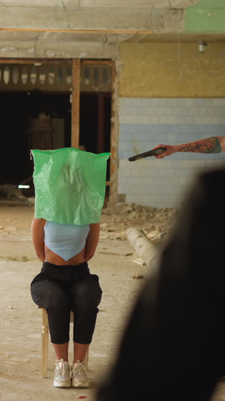 Bandit in mask cocks pistol on woman hostage looking with companion at walking man saver in helmet in old abandoned building slow motion