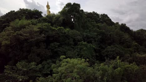 Una-Toma-Aérea-Lenta-Que-Revela-Una-Estatua-De-Buda,-Un-Templo-Y-Campos-A-Lo-Lejos