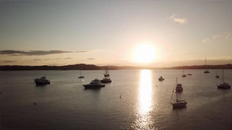 aerial tracking shot towards yachts and boats anchored in the bay of islands as the sun sets