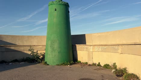 Vista-Frontal-Del-Faro-Verde-Con-Una-Pared-Sobre-Un-Promontorio