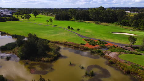 Golfers-teeing-off-onto-golf-course-fairway-under-beautiful-blue-sky-pan-to-lake-and-suburban-community