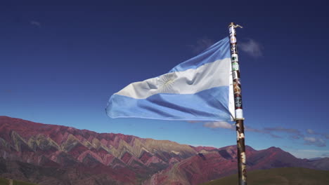 Die-Argentinische-Flagge-Flattert-Im-Wind-Vor-Der-Kulisse-Des-Berühmten-Cerro-De-Los-14-Colores,-Auch-Bekannt-Als-El-Hornocal