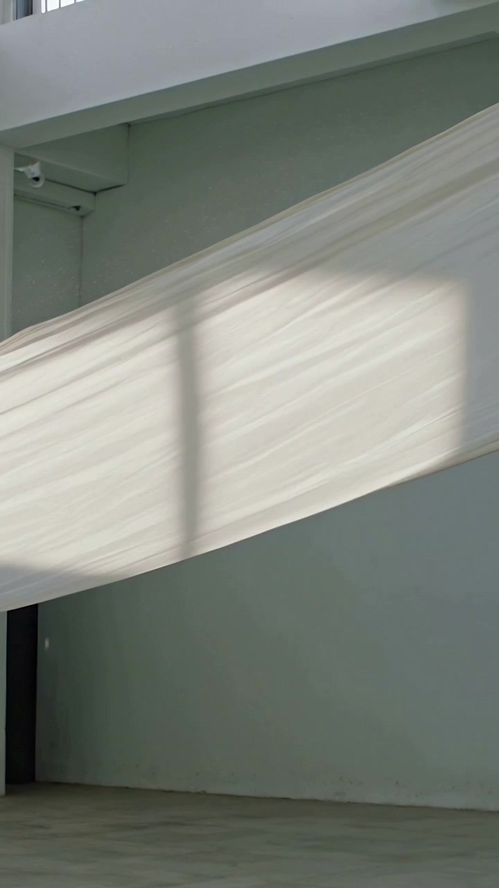 Vertical video: Swaying sheer white fabric slanting across studio as breeze shifting grid shadow