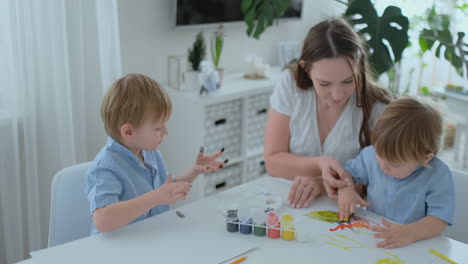 The-family-has-fun-painting-on-paper-with-their-fingers-in-paint.-Mom-and-two-children-paint-with-fingers-on-paper