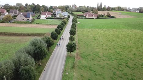 aerial-drone-shot-of-cyclists-driving-on-a-road-in-the-countryside,-near-a-village