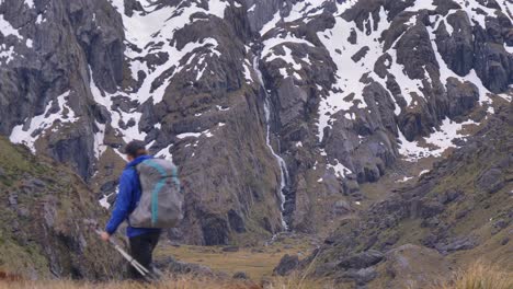 Statik,-Wanderer-Geht-Am-Entfernten-Wasserfall-In-Schneebedeckter-Landschaft-Vorbei,-Routeburn-Track-Neuseeland