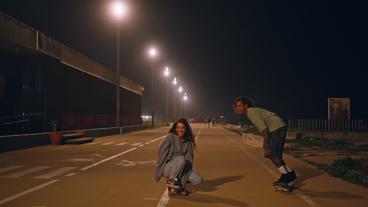 hipsters despreocupados montando patineta en la calle del crepúsculo. patinadores entrenamiento de pareja