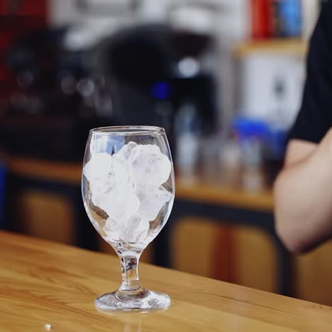 transparent glass with ice cubes. bartender is putting crystal ice cubes in a glass before preparing an alcoholic cocktail to customers on the bar table.