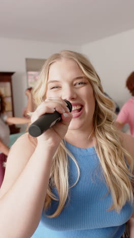 vertical video of caucasian woman singing to microphone with diverse friends dancing, slow motion