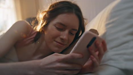 closeup sleepy girl message smartphone in bed. calm awake female checking mobile