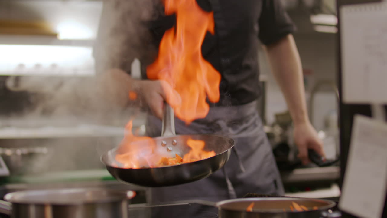 Chef di ristorante che cucina verdure con una grande fiamma in cucina