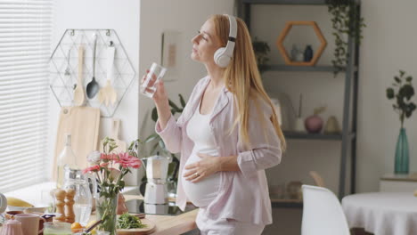 mujer embarazada bebiendo agua y escuchando música en la cocina