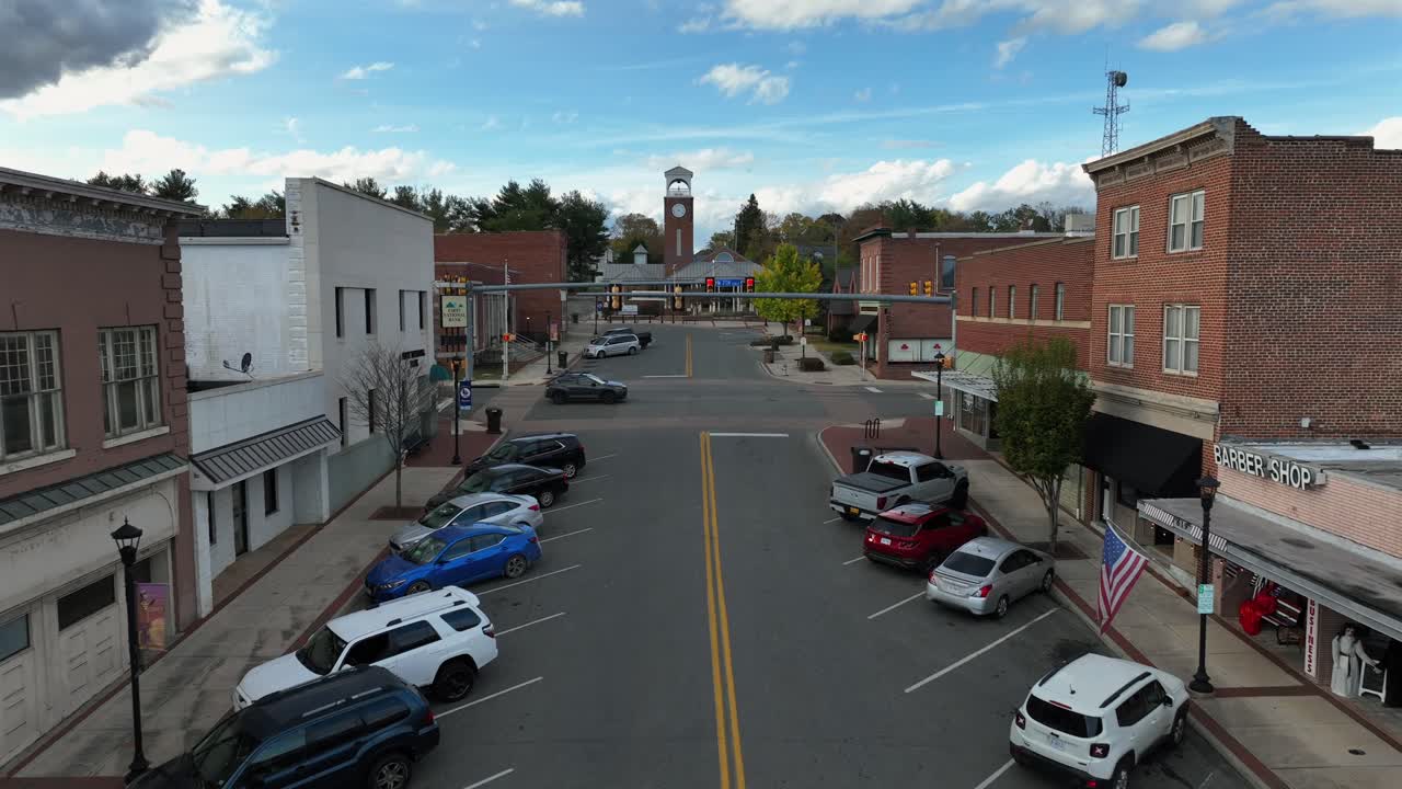 Aerial backwards shot of small american town with church in Background. Traffic lights on junction and parking cars along street. Storefronts in old historic houses. Wide shot. Fall day in USA.