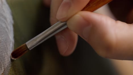 closeup of artists hand holding fine tip paintbrush painting with white oil paint