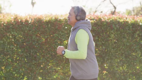 video of senior biracial man in sports clothes and headphones running in street