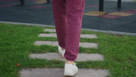 fit enthusiast in hoodie with sport bag slung over shoulder, hands in pockets, walking confidently towards iron exercise bars at outdoor gym near modern apartment buildings under clear sky