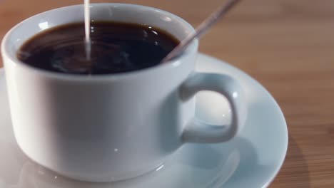 Close-Interior-Slow-Motion-Shot-of-Pouring-Milk-in-a-Black-Coffee-at-Night