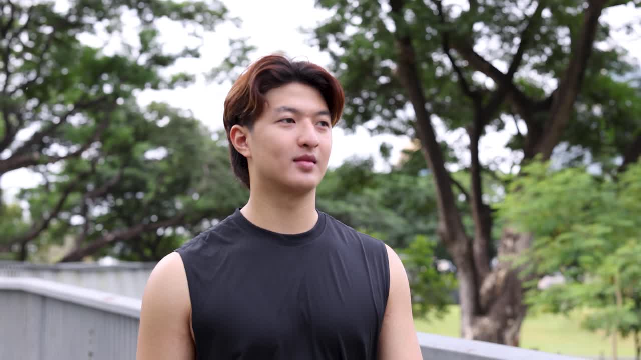 明るい日中のフィットネス活動中に、若いアジア人男性が公園の橋を歩いている。