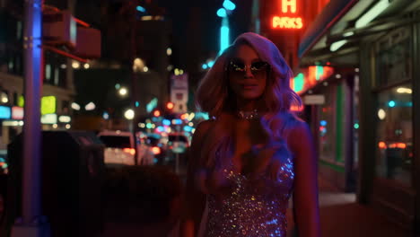 blonde woman in sparkling dress walking through a neon-lit city at night
