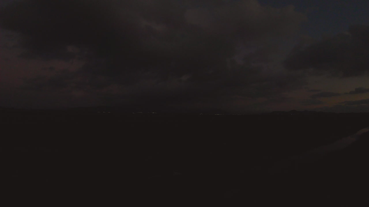 Sunset clouds range in colors from warm to cool as they form over an airport runway. A small stream is in the foreground, it reflects the sunsets beauty.