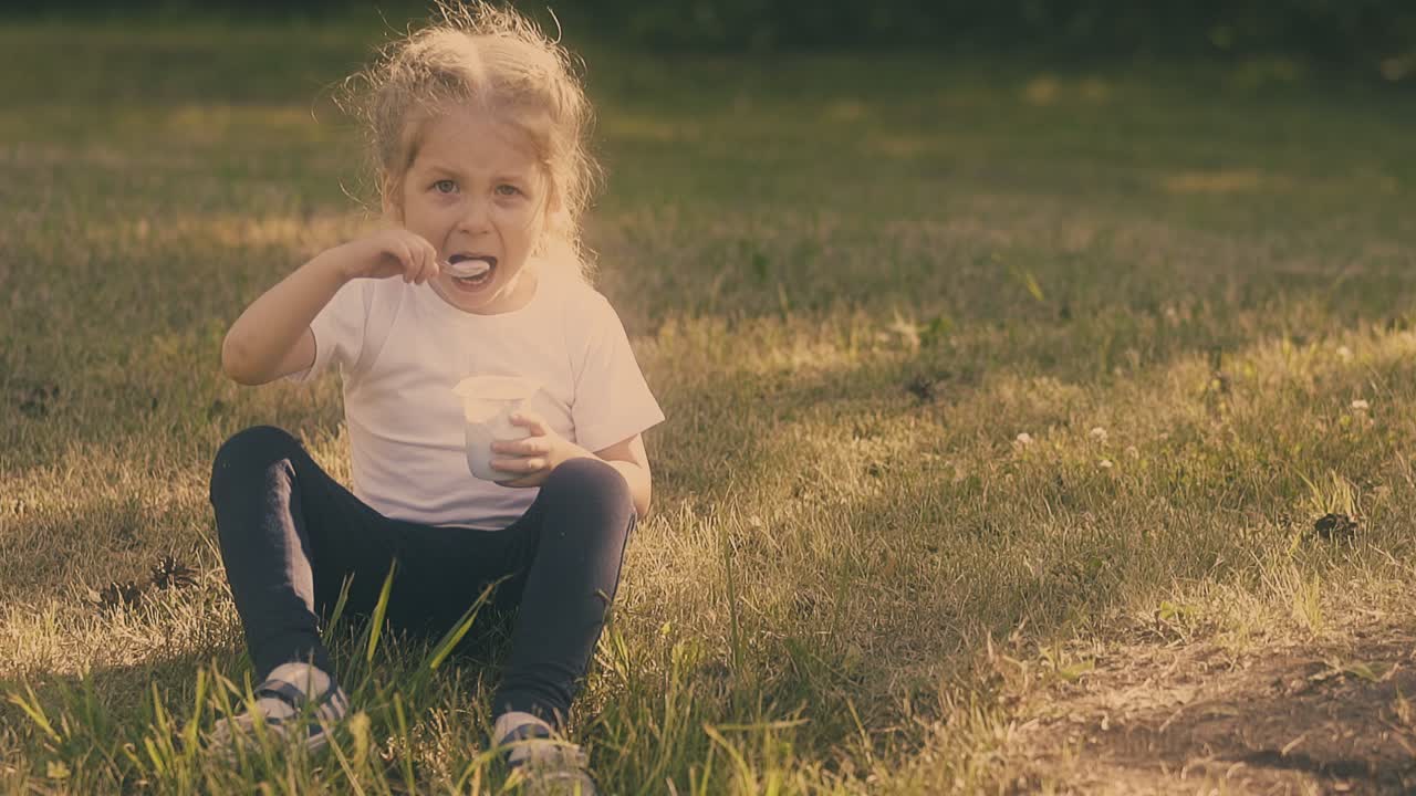 girl with braids wearing white t-shirt enjoys eating yogurt