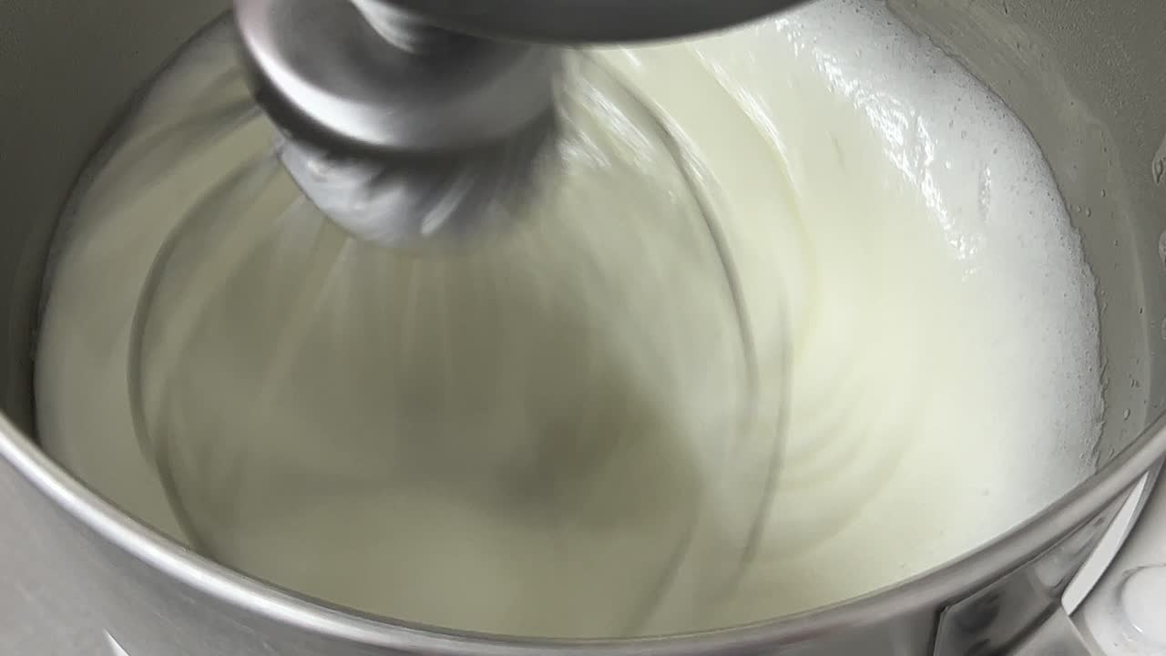 Delicious meringue buttercream making in progress, whipped egg white mixing in the heavy duty mixer, close up shot in commercial bakery setting