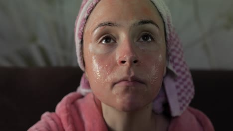 woman watching a late night movie at tv, eating popcorn. bathrobe, facial mask