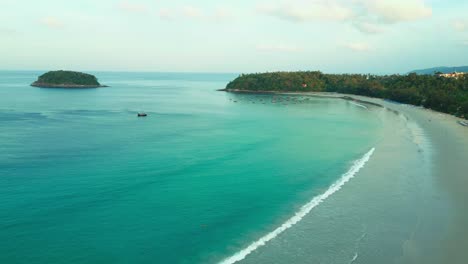 crystal-clear waters meet soft white sand on this tranquil thai beach, curving gently toward a forested headland with a small island in the distance—pure tropical serenity.