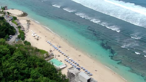 from the edge of the hill in uluwatu bali, melasti beach is visible, along with various hotels and sunshades, and a large number of people who are either strolling on the beach or swimming in the sea