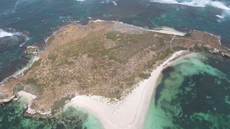 Ripresa aerea dall'alto di un'isola deserta australiana con onde che si infrangono sotto la luce del sole.