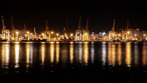 a stunning night view of a port with illuminated cranes and reflections on water, showcasing the vibrant activity and serene beauty of a shipping dock after sunset
