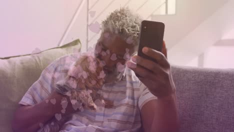 Animation-of-falling-hearts-over-african-american-senior-man-using-smartphone