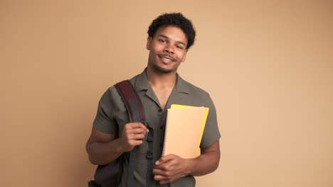 happy male university student with backpack and books in beige studio