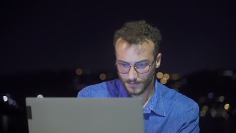 Man-working-intensely-on-laptop-at-night-by-the-sea.