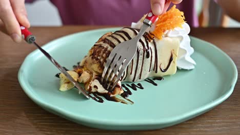 woman cutting a banana cold crepe cake before eating.