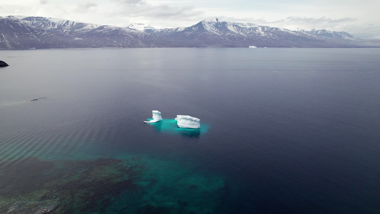 Aerial View of Small Iceberg Calving in the Arctic, Mountains in the Background - Boom Down Shot