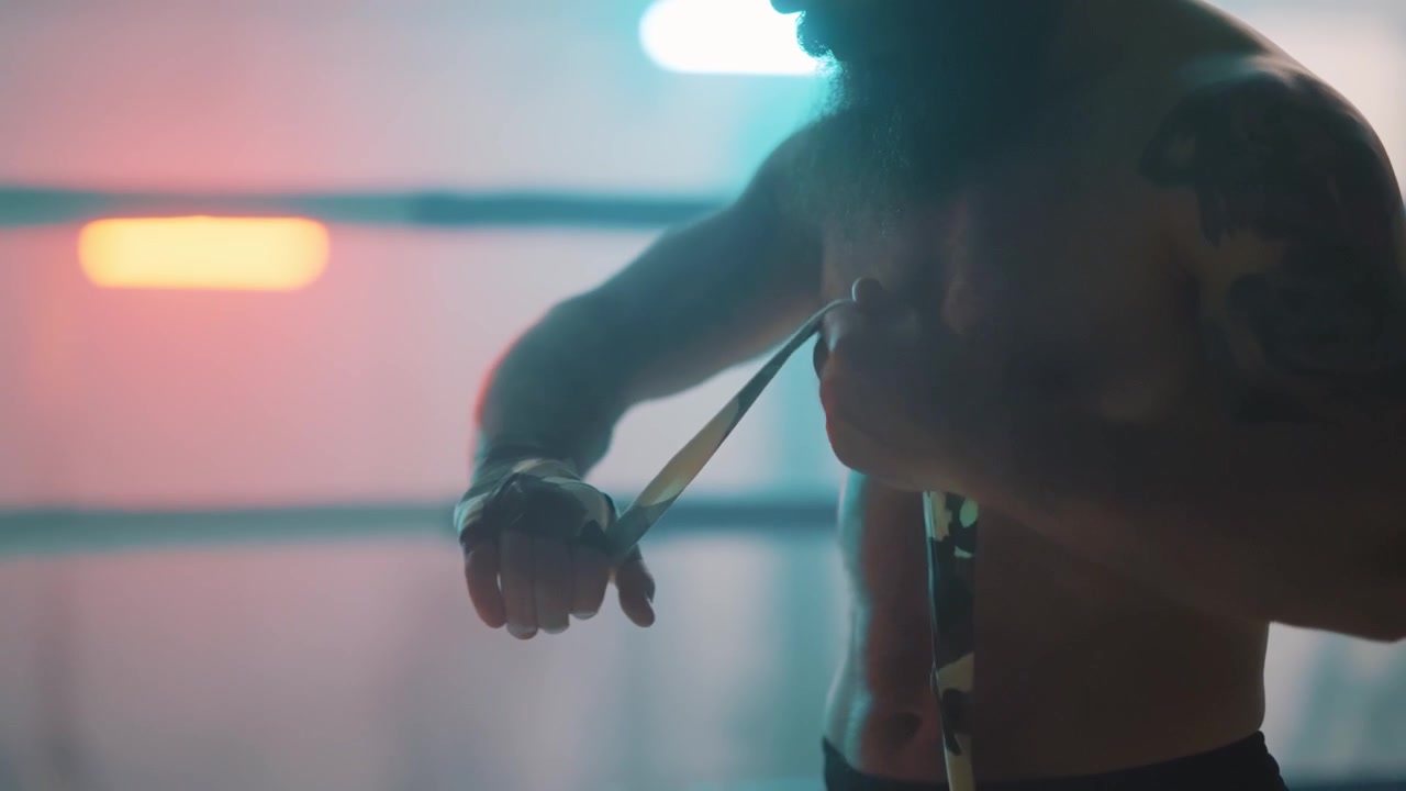 Combattente barbuto che si fascia le mani in un ring da boxe illuminato al neon