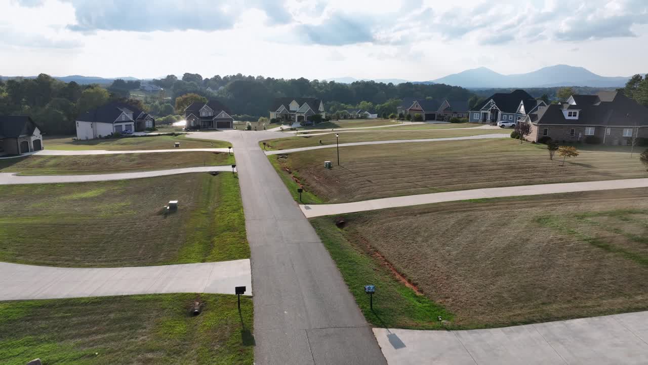 Aerial flyover street of new developed residential area in suburb of town. Sunny late summer day with dried grass in front yards. Long driveway to upper class single family houses in Virginia