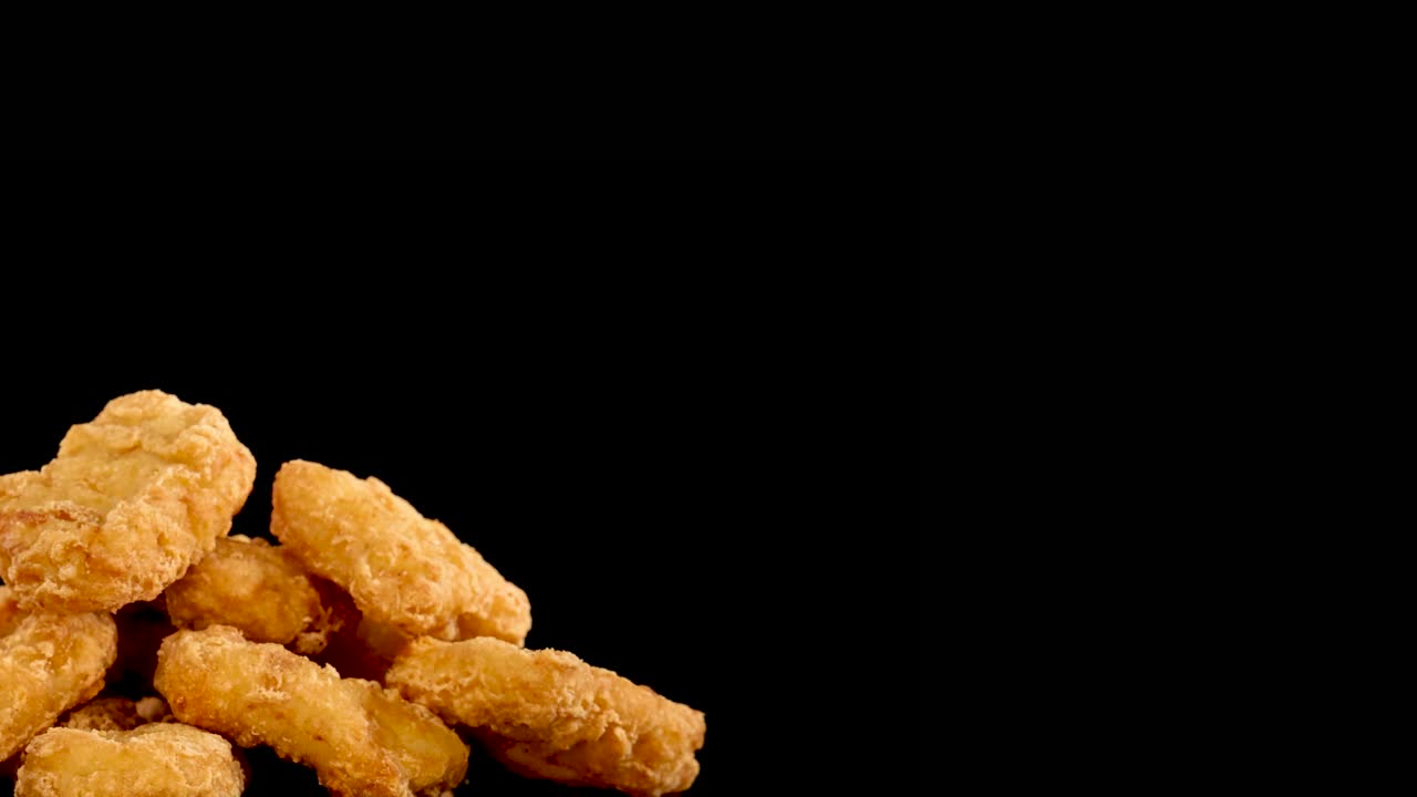 Golden, crumbed chicken nuggets spin slowly in close-up against a black background, highlighting crispy texture and warm lighting with copy space on the right