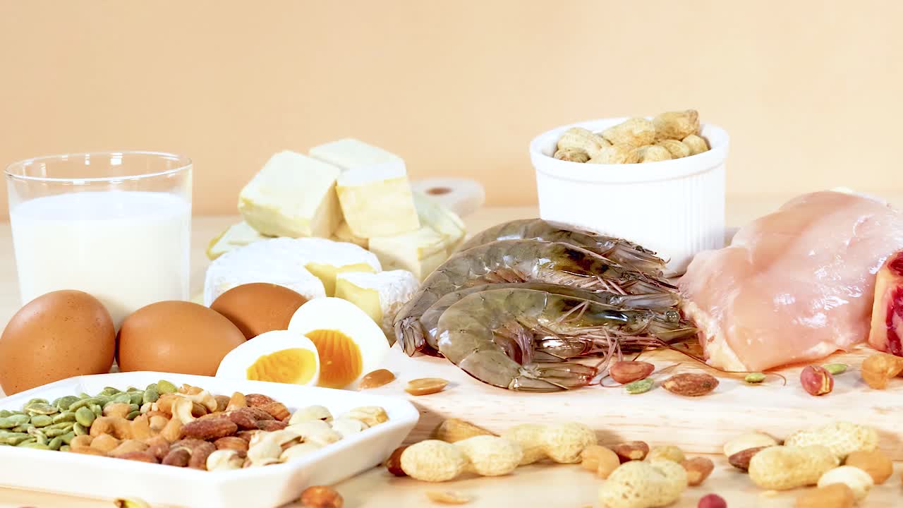 A variety of protein-rich foods including meats, nuts, and dairy are artfully arranged on a wooden surface