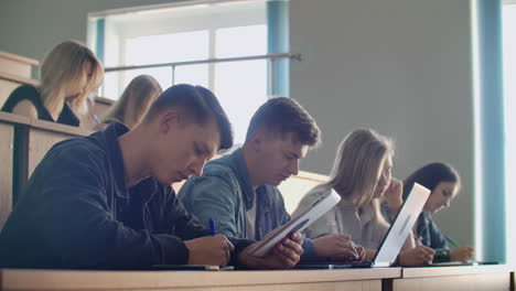 eine gruppe von leuten an der universität hört sich einen vortrag an und schreibt einen abstract in ein notizbuch hinter einem college-professor.