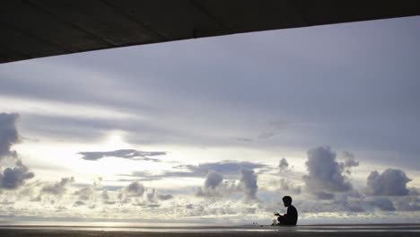 A-boy-sits-under-the-friendship-bridge-in-Koror,-Palau-at-sunset-on-a-cloudy-day