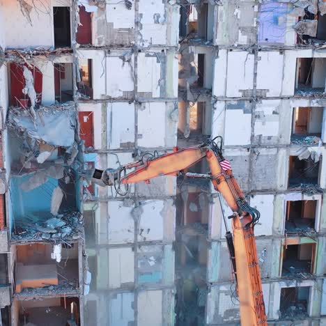 excavator grabber reaches high to dismantle the walls of an old building. parts of concrete and heavy dust falling down. construction excavators are clearing the ruins of an old building