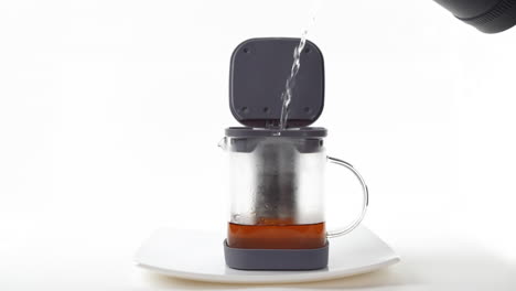 a hand pouring hot water into a french press coffee maker on a white background